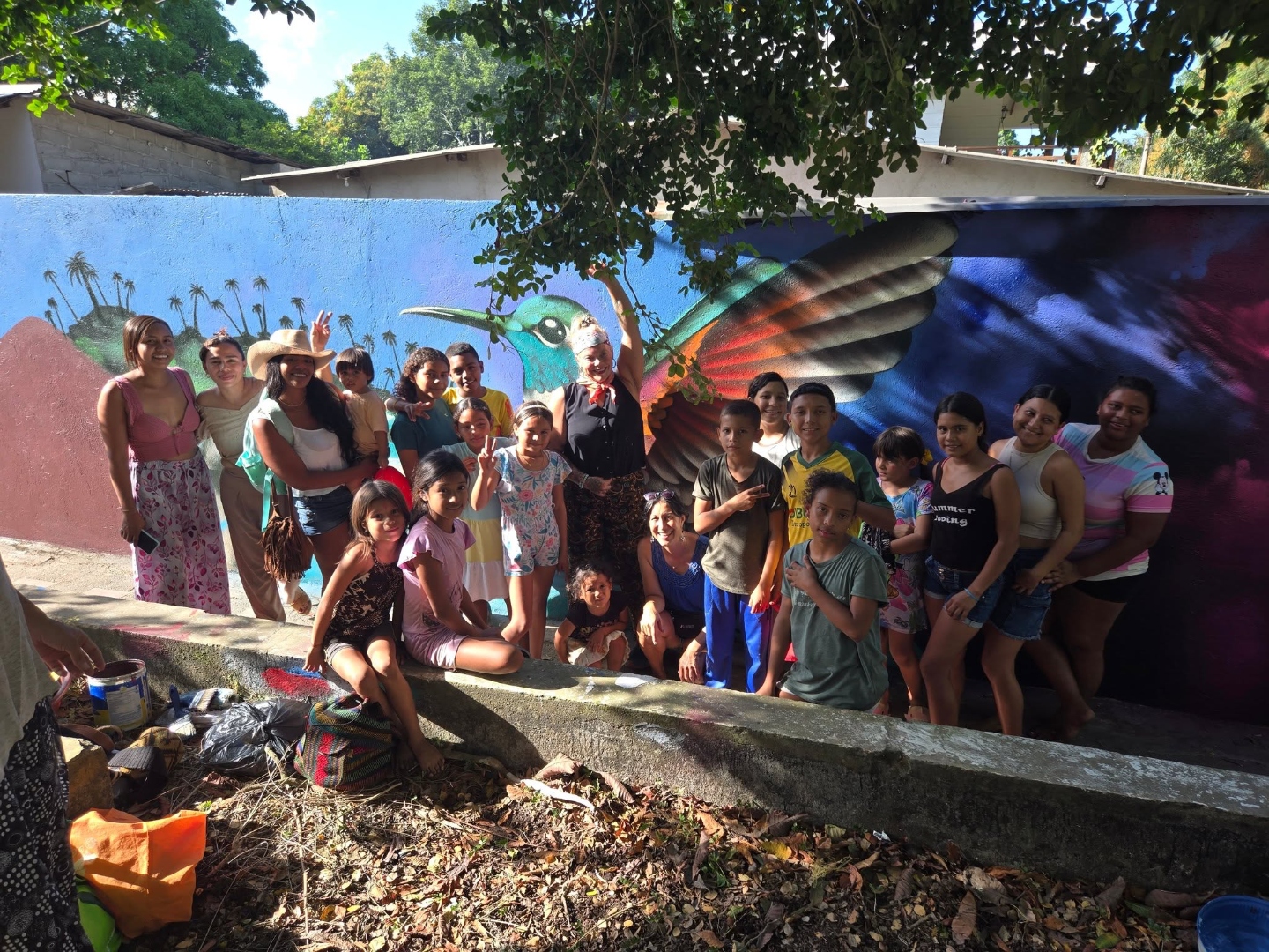 Community gathered in front of a vibrant hummingbird mural painted together in the village